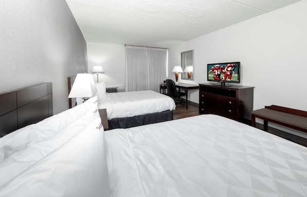 A hotel room with two beds, a desk, a television, and a bench.