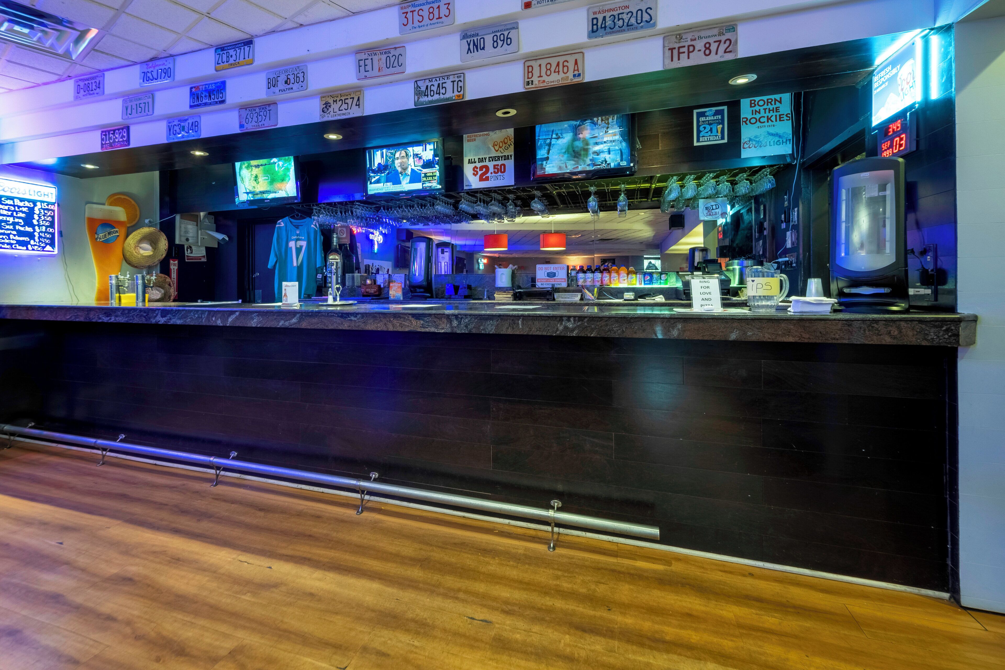 A bar area with multiple televisions displaying sports events, a variety of bottles and glasses, and a wooden floor.