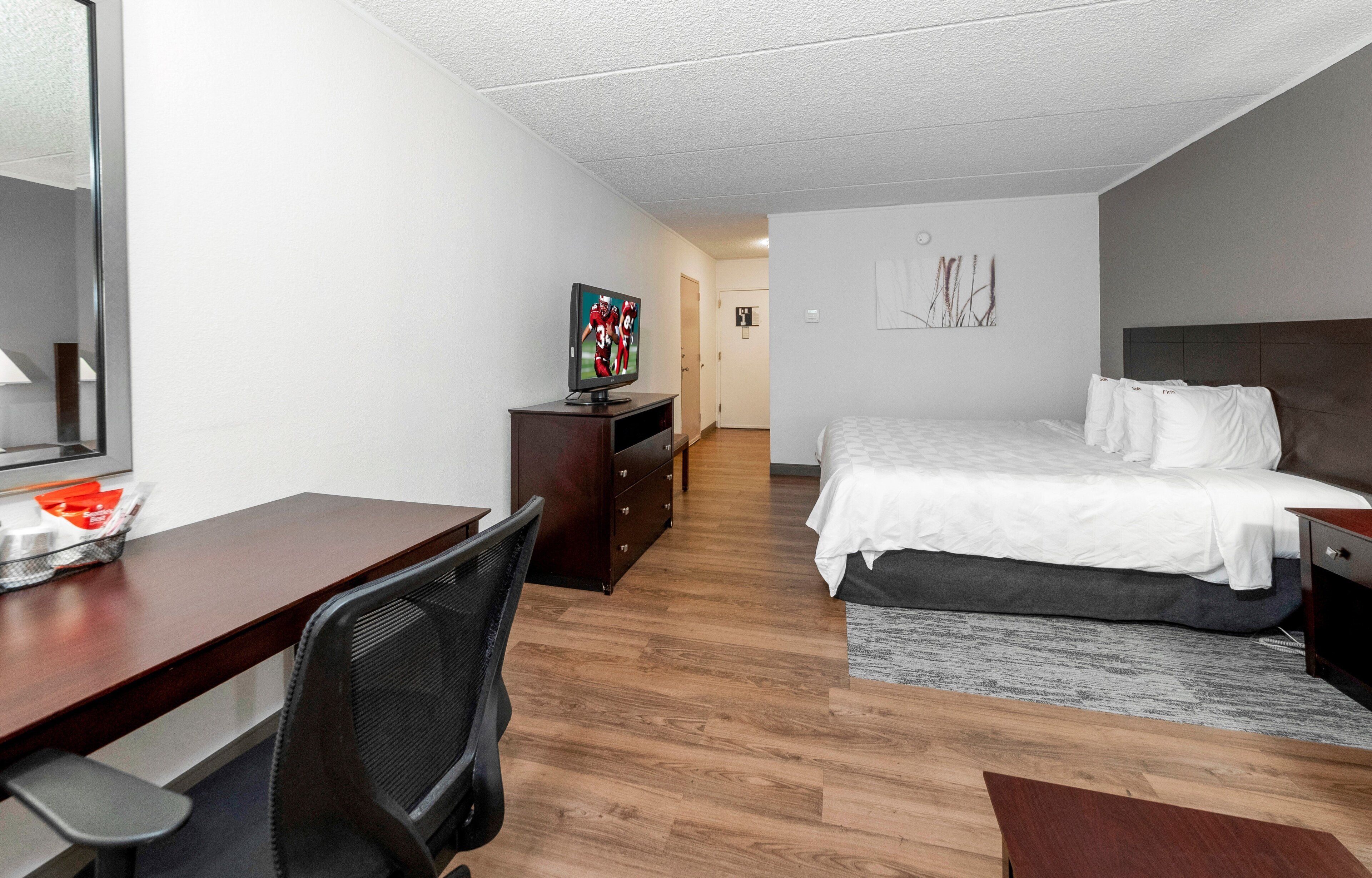 A hotel room with a bed, a desk with a chair, a television, and a small cabinet.