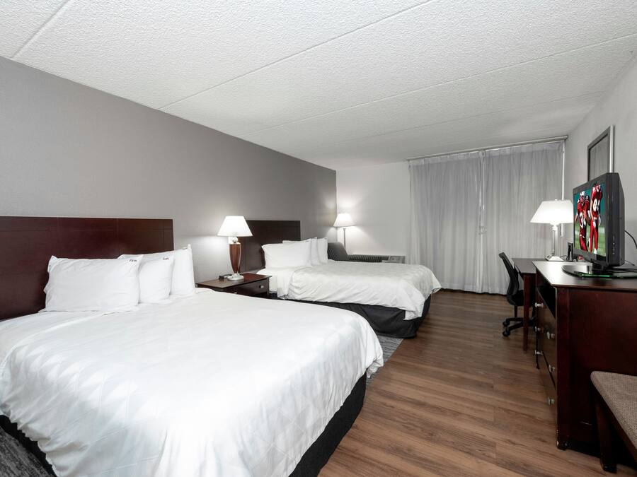 Habitación de hotel con dos camas, un escritorio, una silla, un televisor y una ventana con cortinas.