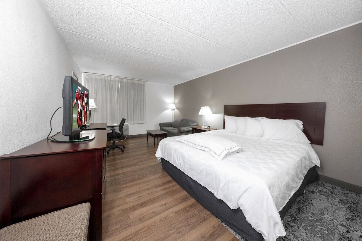 A hotel room with a bed, desk, chair, and a television.