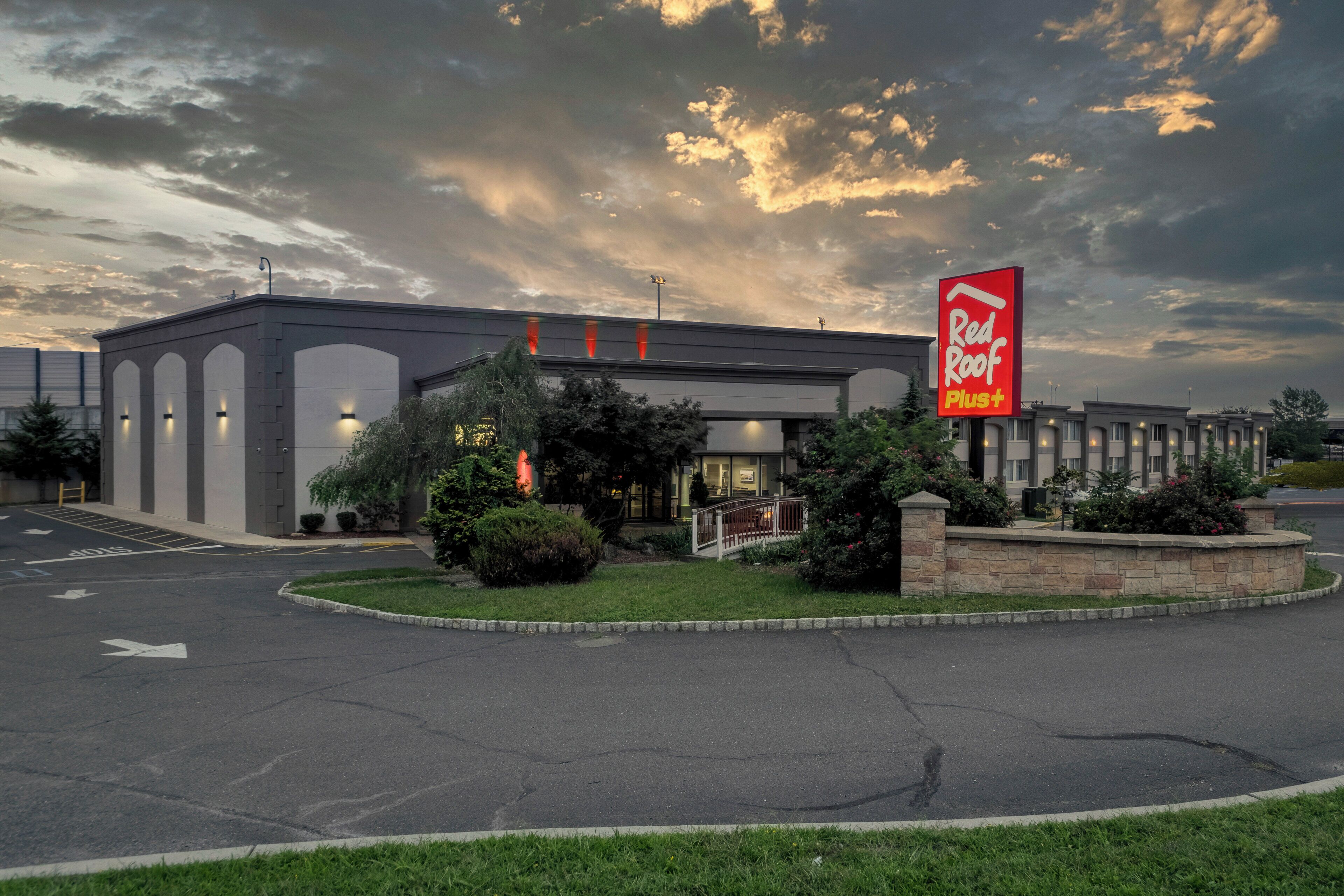 A Red Roof Plus hotel with a parking lot and a landscaped area in front.