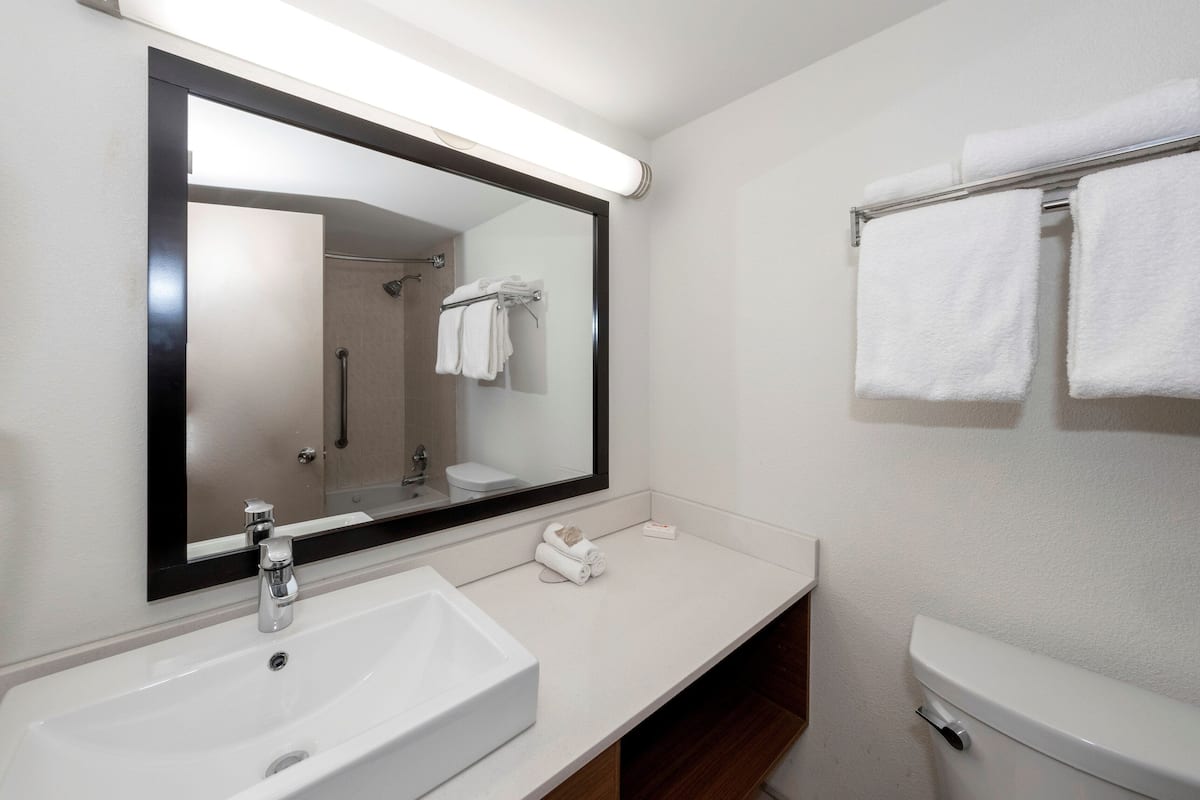 A modern bathroom with a large mirror, white sink, and a towel rack with folded towels.