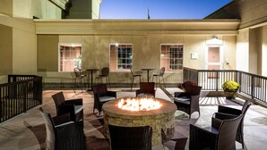 An outdoor patio area with wicker furniture, a central fire pit, and a view of the building's exterior.