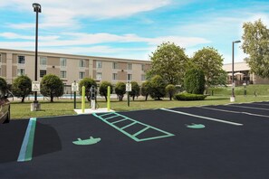 Un área de estacionamiento con estaciones de carga para vehículos eléctricos, una señal de estacionamiento reservado y un edificio al fondo.