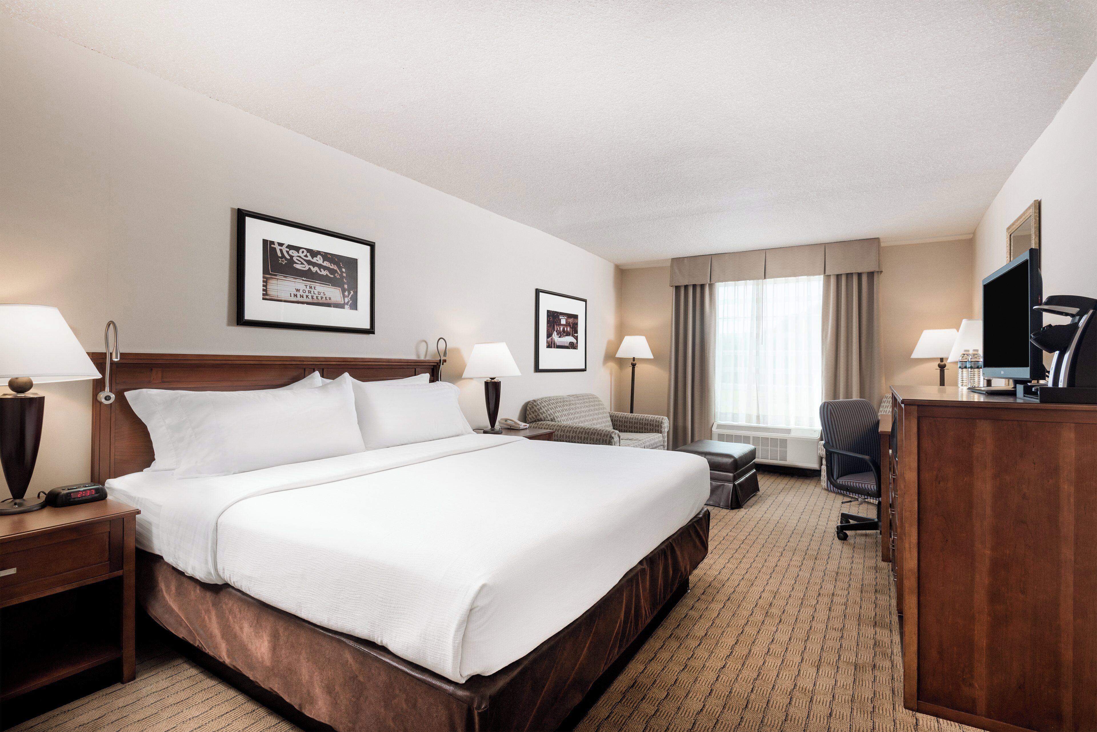 A hotel room with a large bed, two bedside tables, a desk, a chair, a television, and two framed pictures on the wall.
