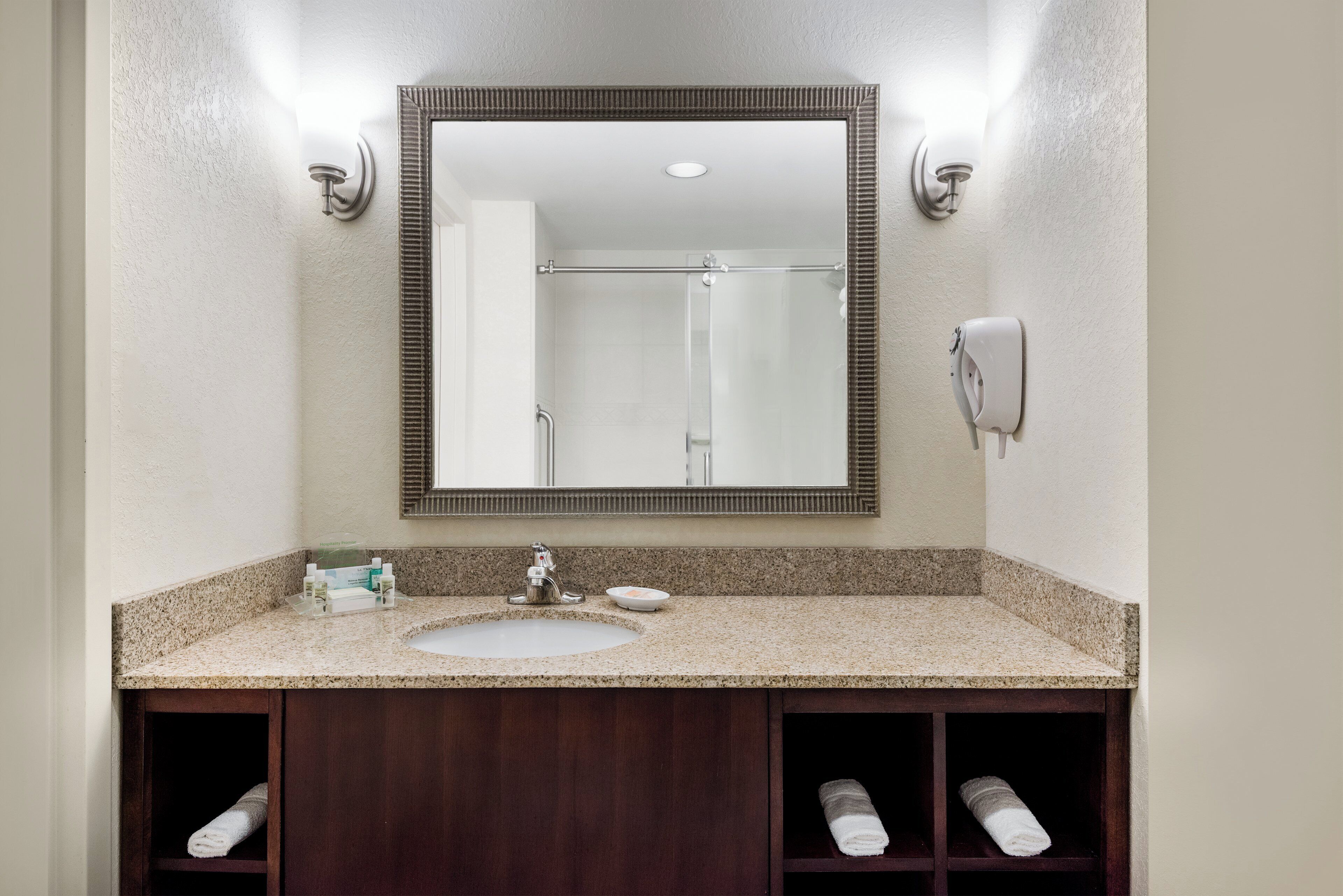 A bathroom with a sink, mirror, towel rack, and a handheld showerhead.