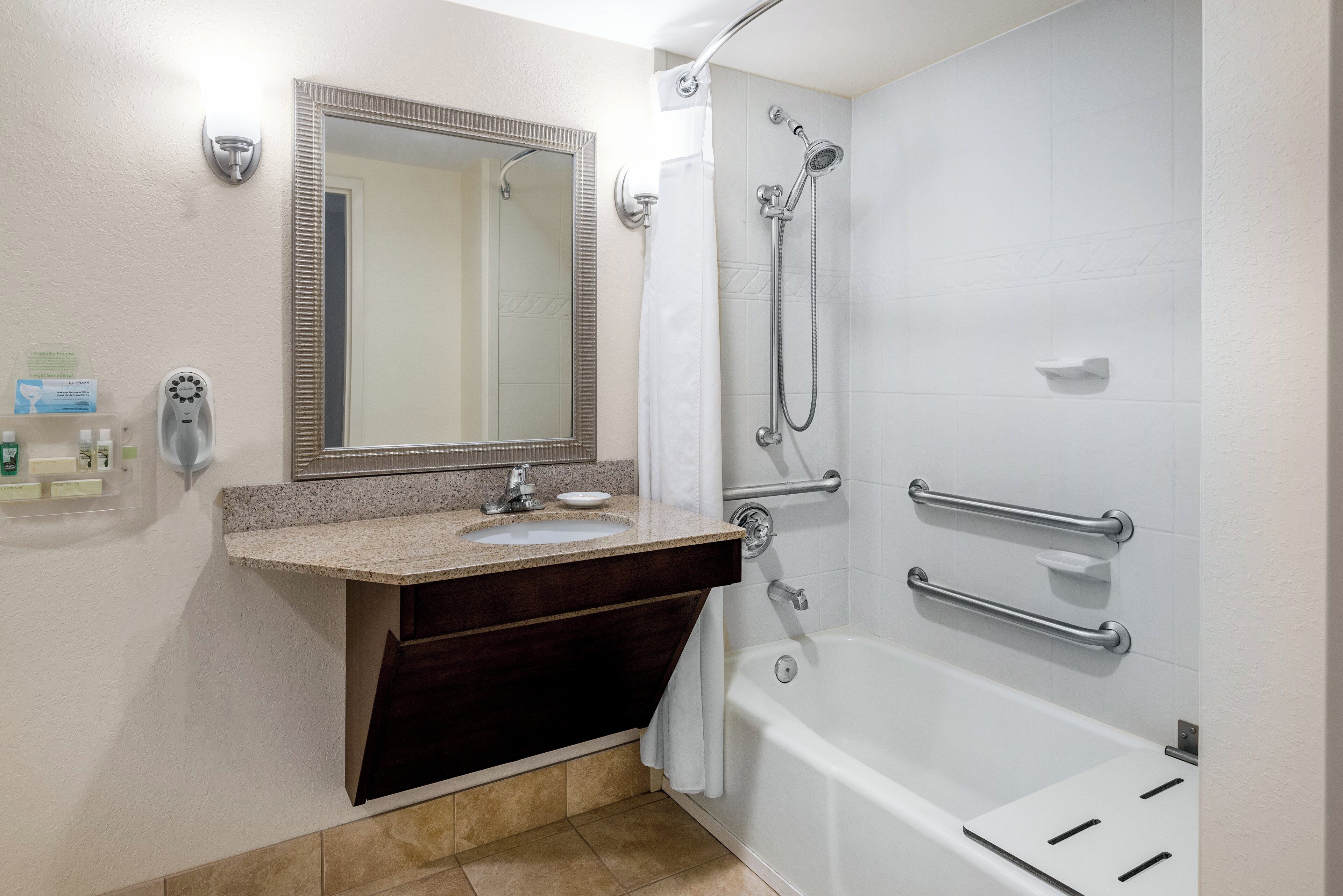 A bathroom with a sink, mirror, shower, and grab bars.