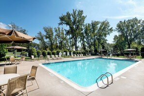 A swimming pool with lounge chairs and umbrellas, surrounded by trees. - Holiday Inn Johnstown-Gloversville by IHG (Johnstown)