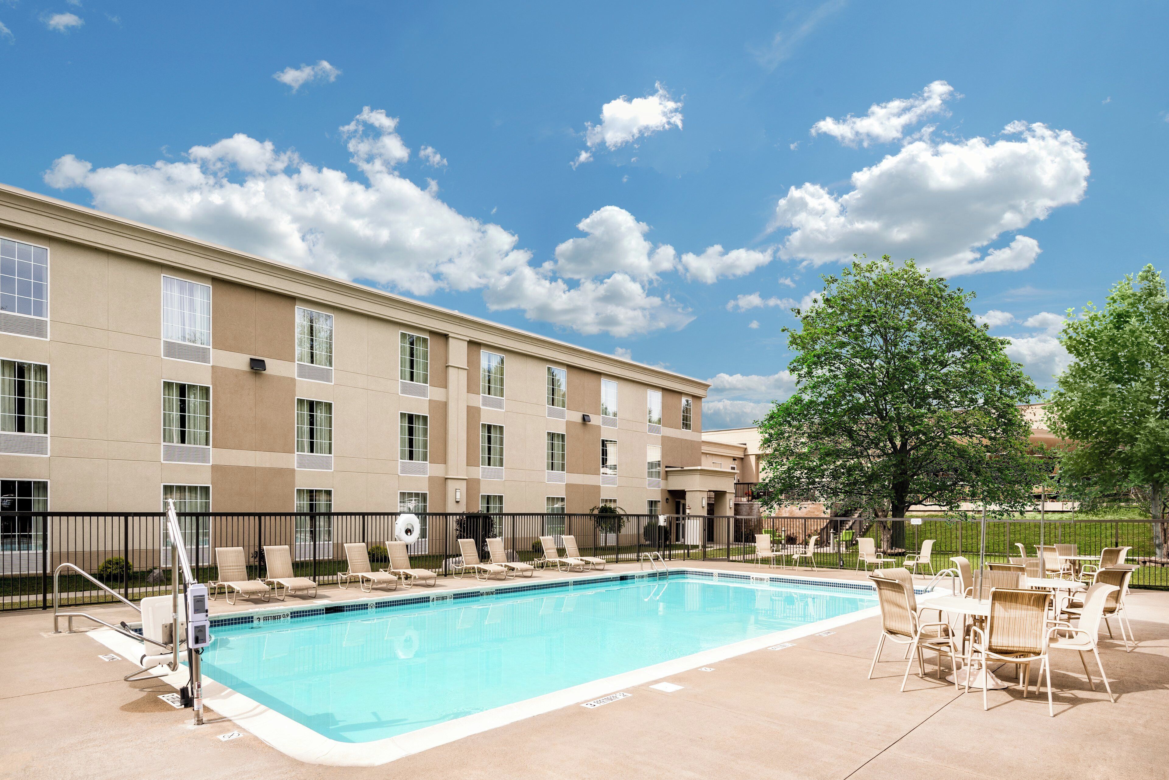 A hotel with a swimming pool, lounge chairs, and a large tree.