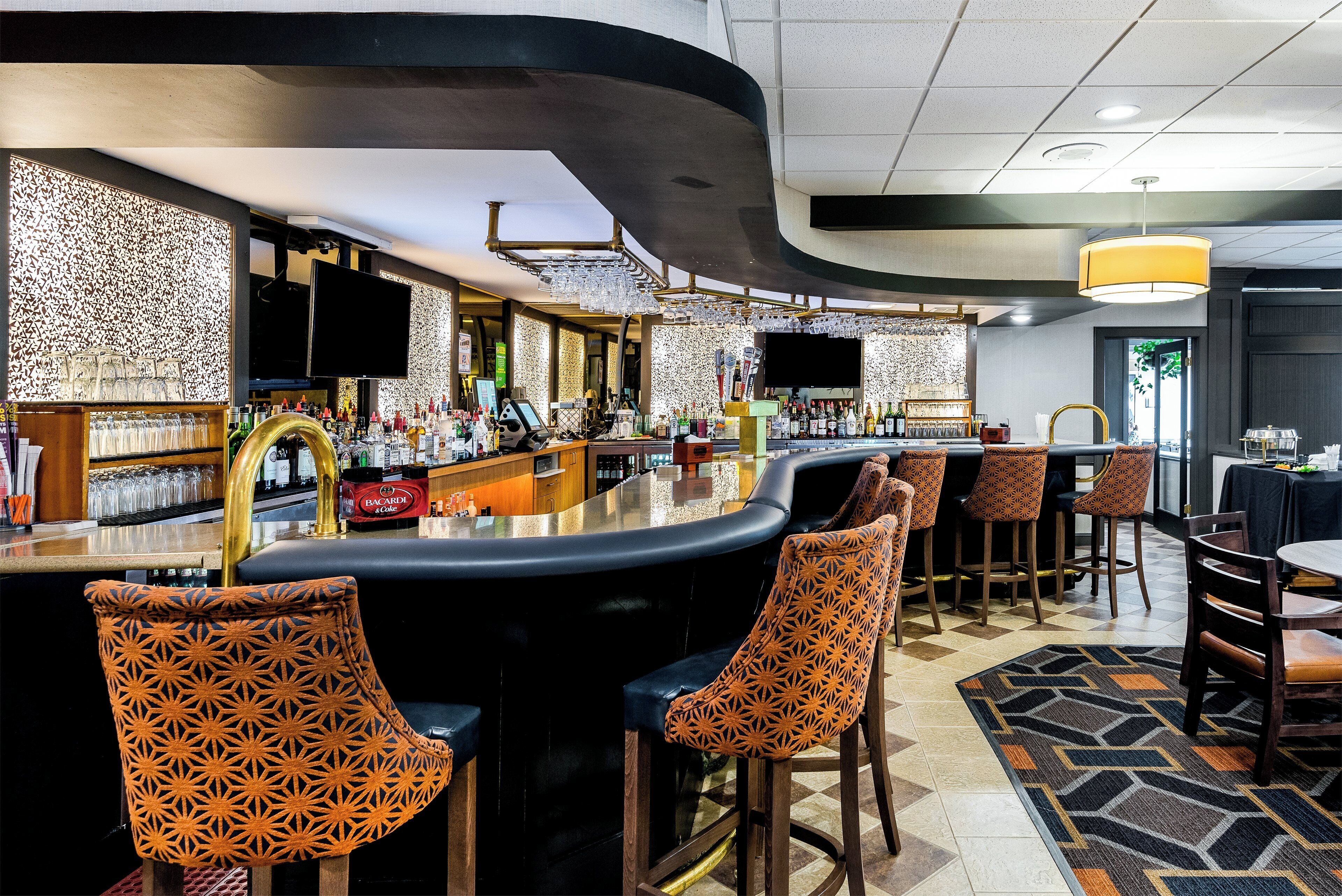 A bar area with a curved counter, multiple bar stools, and a television screen.
