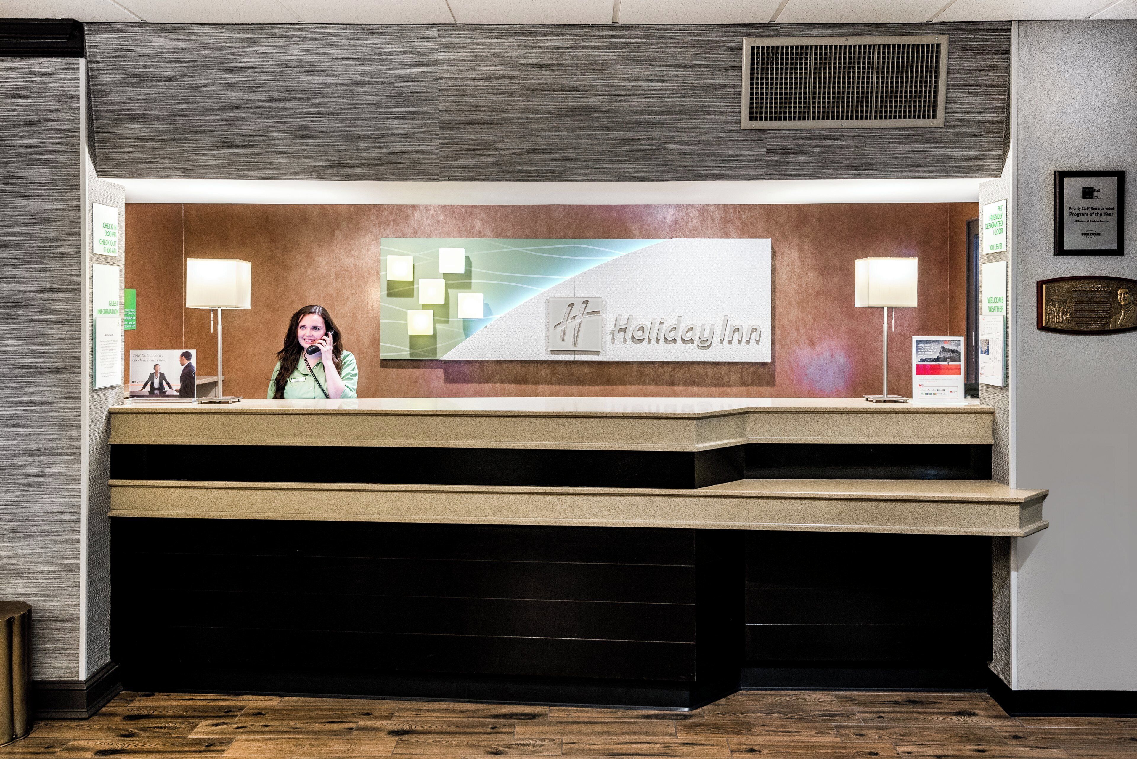 Een receptiebalie met een 'Holiday Inn' bord, een informatiebord voor gasten en een 'Priority Club' plaquette.