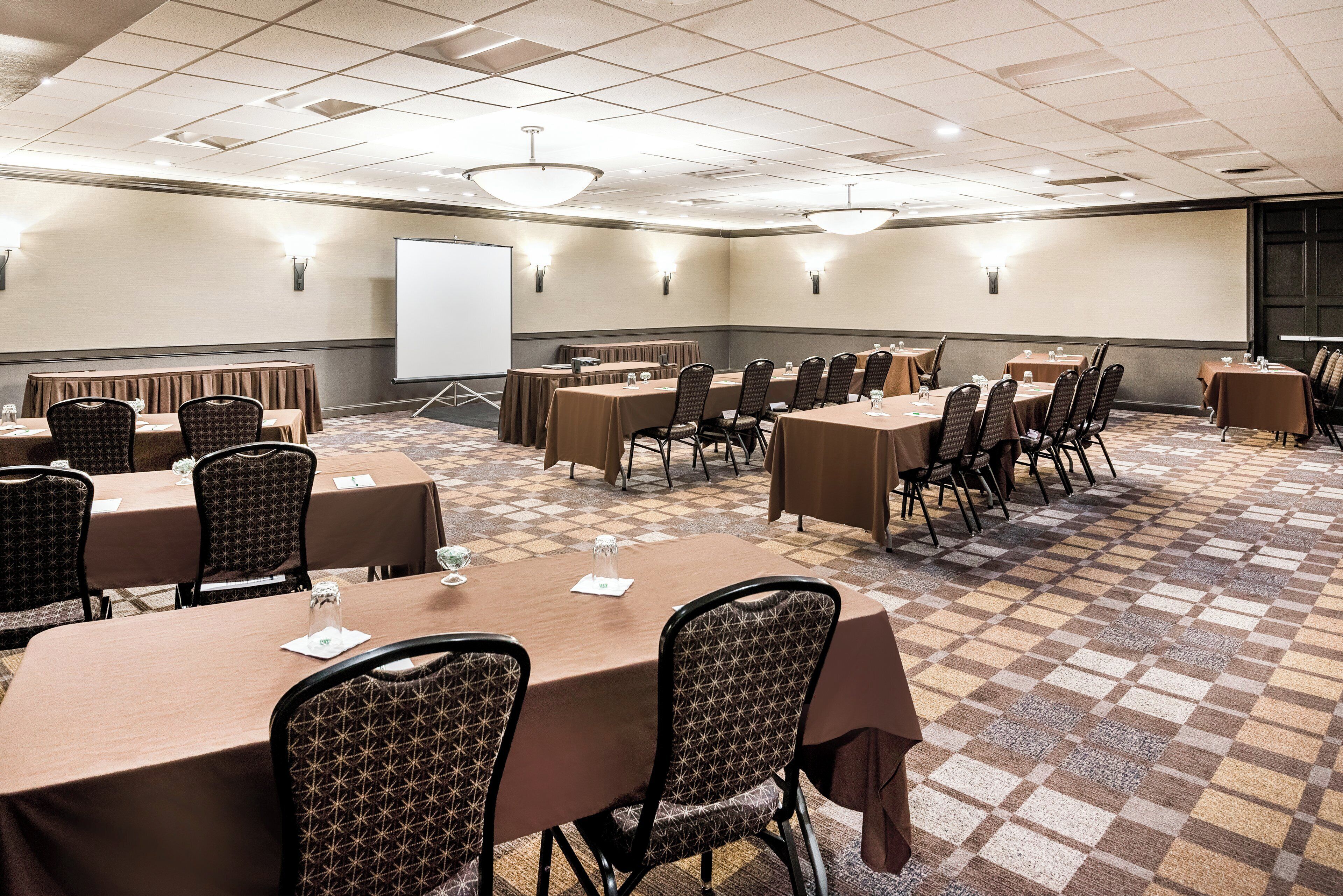 Un salón de conferencias con varias mesas y sillas, una pizarra y una pantalla de proyector.