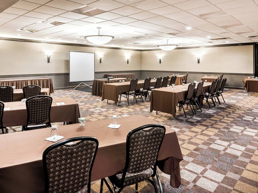Une salle de conférence équipée de plusieurs tables et chaises, d’un tableau blanc et d’un écran de projection.