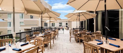 Eine Terrasse mit Sitzgelegenheiten, Sonnenschirmen und Blick auf das Gebäude im Hintergrund.