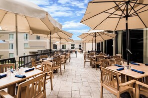 A terrace with outdoor seating, umbrellas, and a view of the building in the background. - Holiday Inn Johnstown-Gloversville by IHG (Johnstown)
