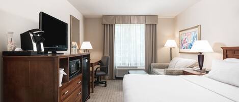Habitación de hotel con cama, escritorio con computadora, televisión, cafetera y ventana con cortinas.