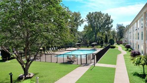 A swimming pool surrounded by a fence, with a grassy area and a building in the background. - Holiday Inn Johnstown-Gloversville by IHG (Johnstown)