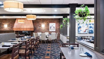 A restaurant with brick walls, hanging pendant lights, and a patterned carpet.