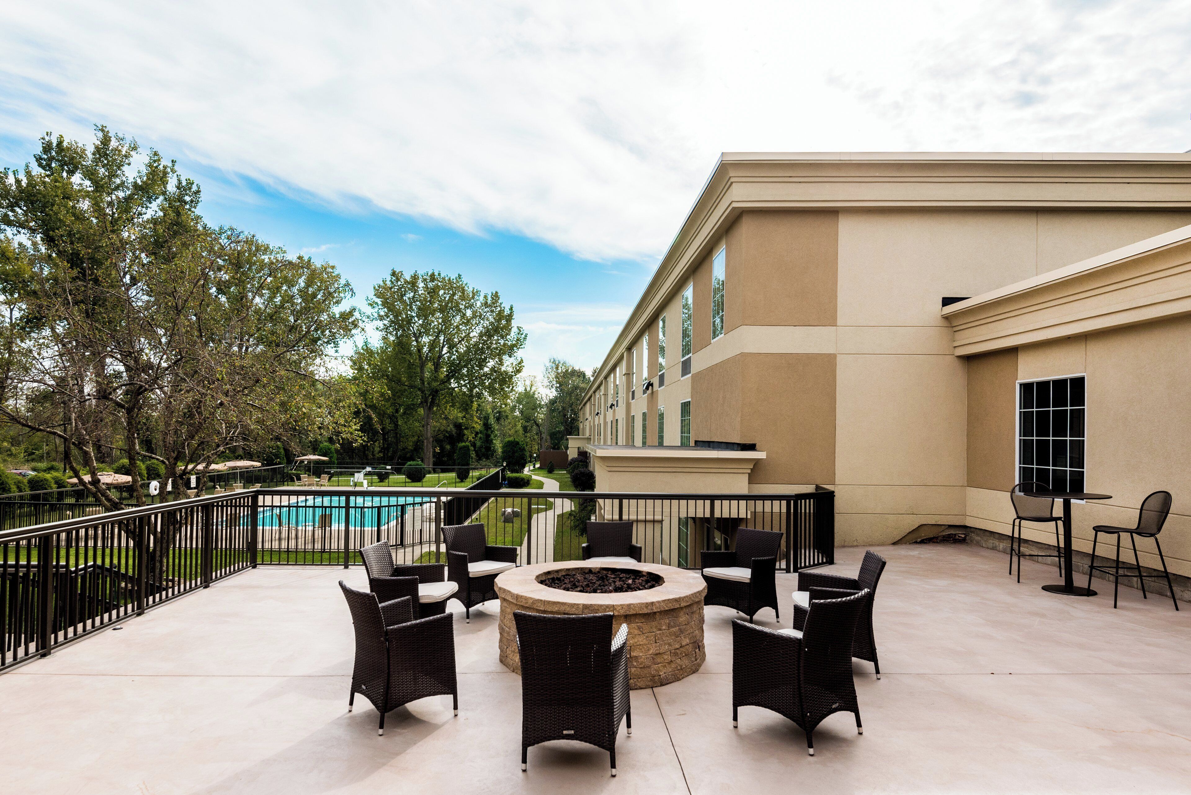 Un patio exterior con mobiliario de mimbre, un pozo de fuego y vistas a una piscina y un edificio.