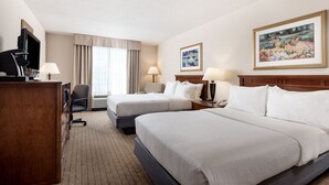 A hotel room with two beds, a desk, a TV, and a painting on the wall.