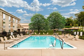Relax by the pool surrounded by lounge chairs and umbrellas, with a lifeguard stand nearby for added safety.