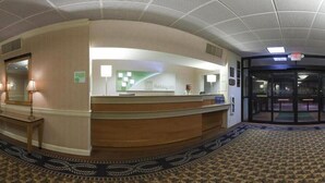 A hotel reception area with a counter, a reception desk, a waiting area with a patterned carpet, and a revolving door.