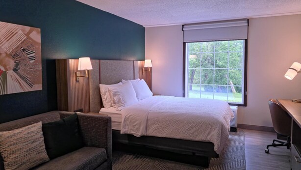 A hotel room with a bed, a sofa, a desk, and a large window.