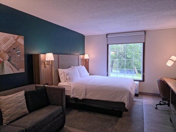 A hotel room with a bed, a sofa, a desk, and a large window. - Holiday Inn Johnstown-Gloversville by IHG (Johnstown)