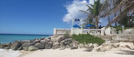 A beach with a white fence, blue umbrellas, and a sign.