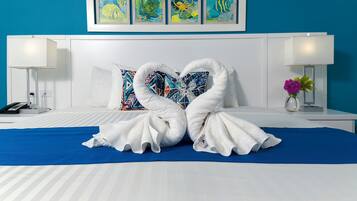 A hotel room with a bed, two white towels arranged in a heart shape, a blue bedspread, and a wall with colorful artwork.