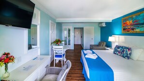 A hotel room with a bed, a desk, a chair, a TV, and a painting on the wall. - Dover Beach Hotel (St. Lawrence Gap)