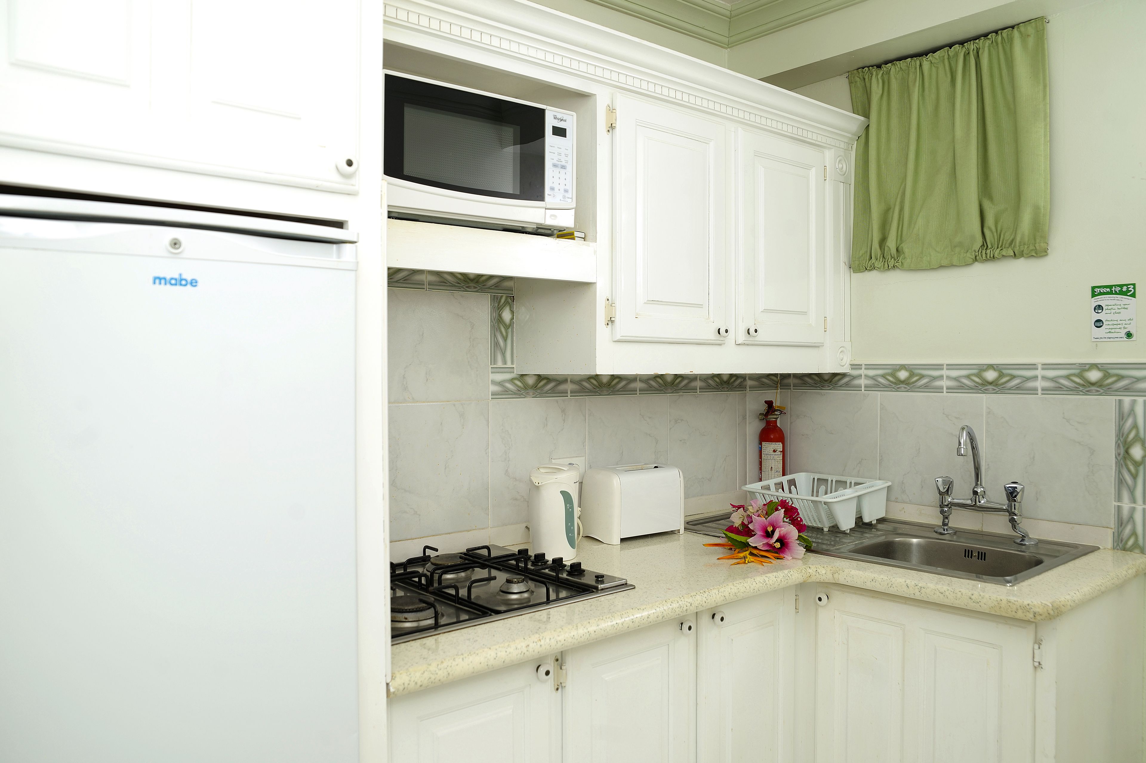 Una cucina con mobili bianchi, un forno a microonde, un tostapane, un lavandino e una stufa a gas.