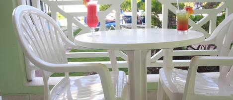 A white plastic table and chairs set on a balcony with a view of palm trees and a blue umbrella.