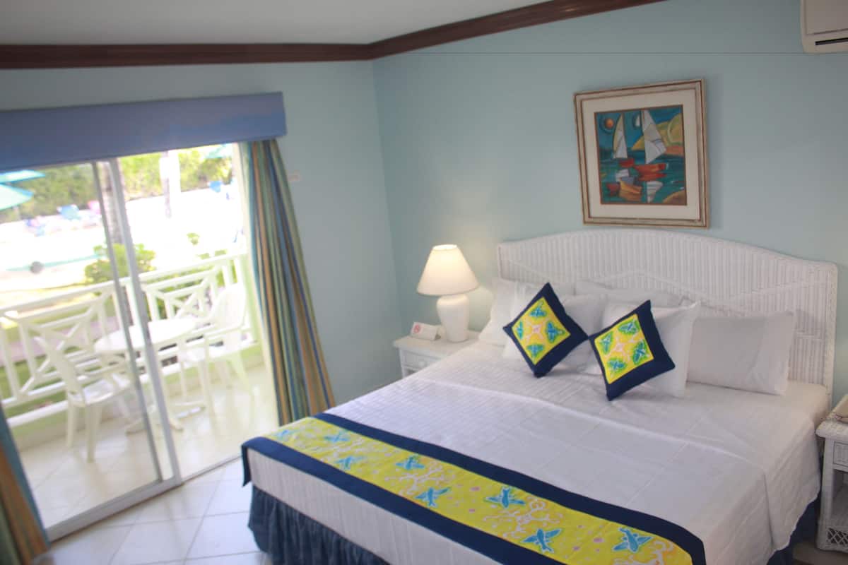Habitación de hotel con cama, mesita de noche, lámpara, un cuadro y vistas al exterior.