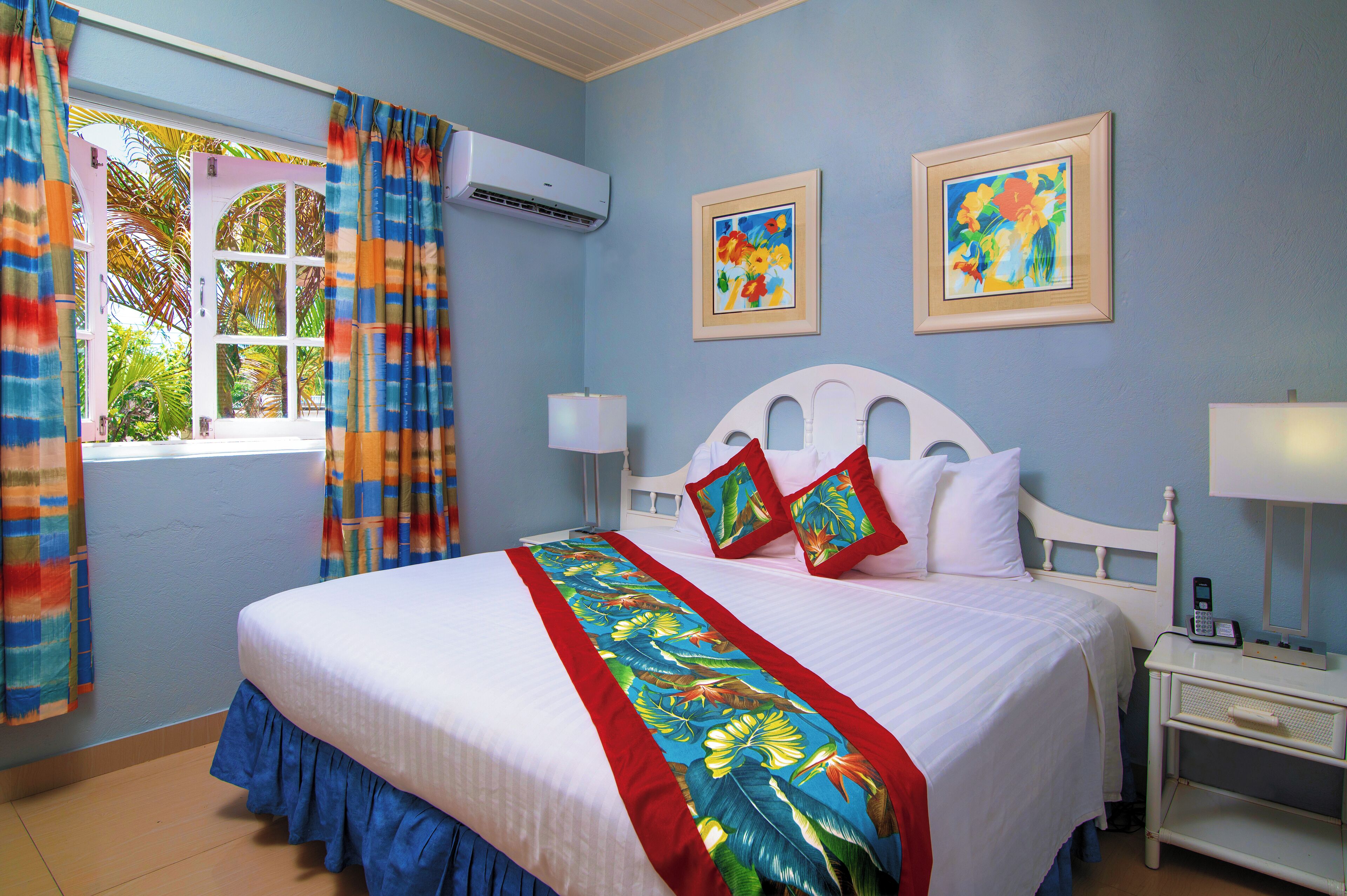 Habitación de hotel con cama, mesita de noche, cortinas en una ventana y dos cuadros colgados en la pared.