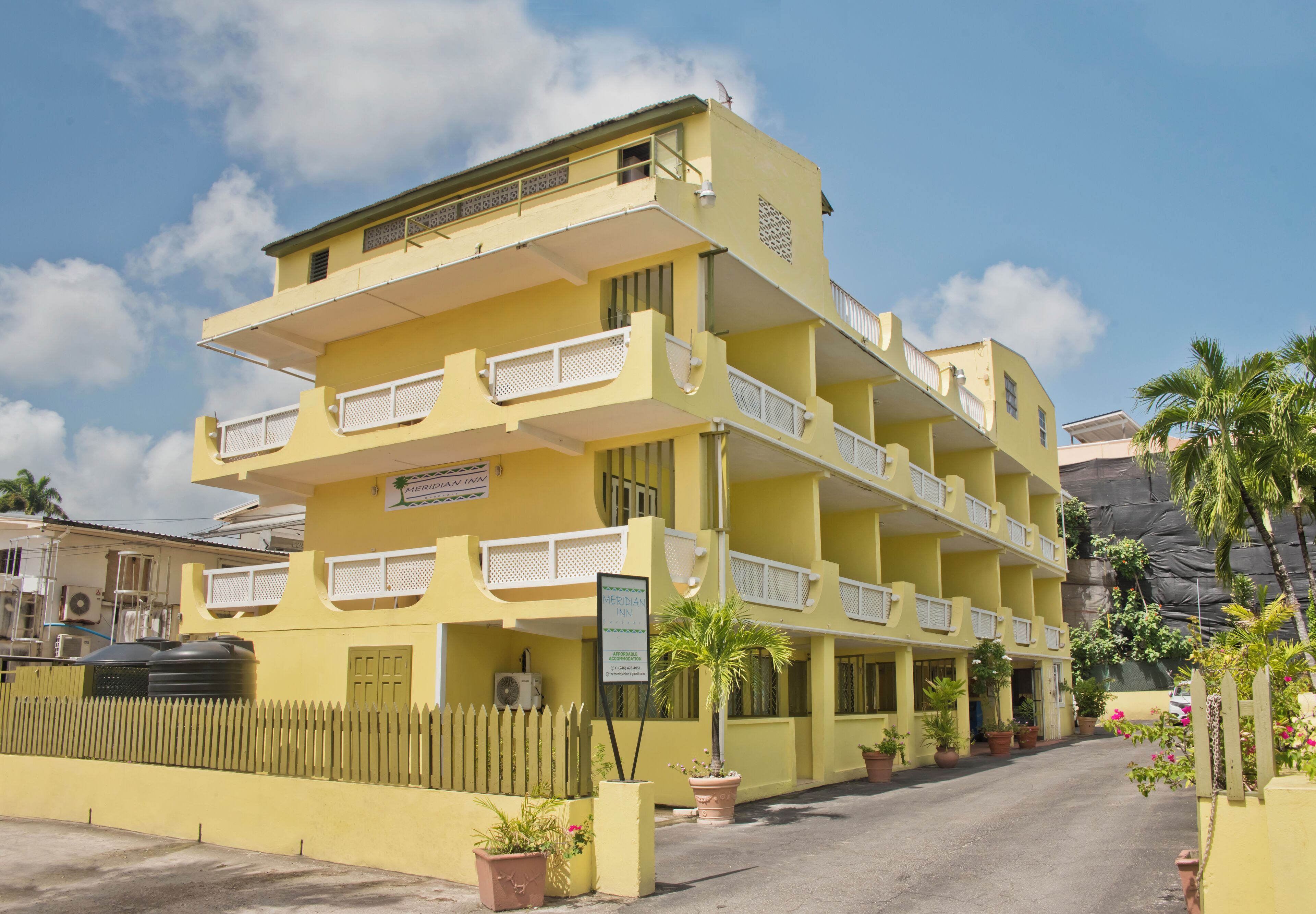 A multi-story yellow building with balconies, a signboard, and potted plants.