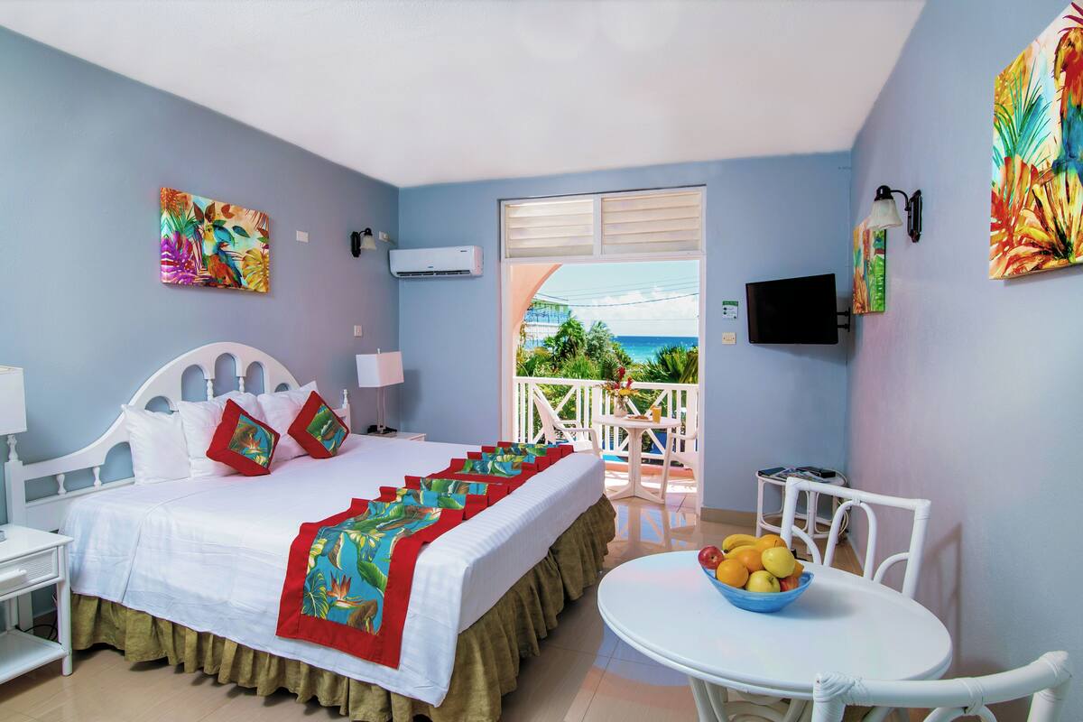 Habitación de hotel con cama, balcón con vistas, televisión y una mesa con fruta.