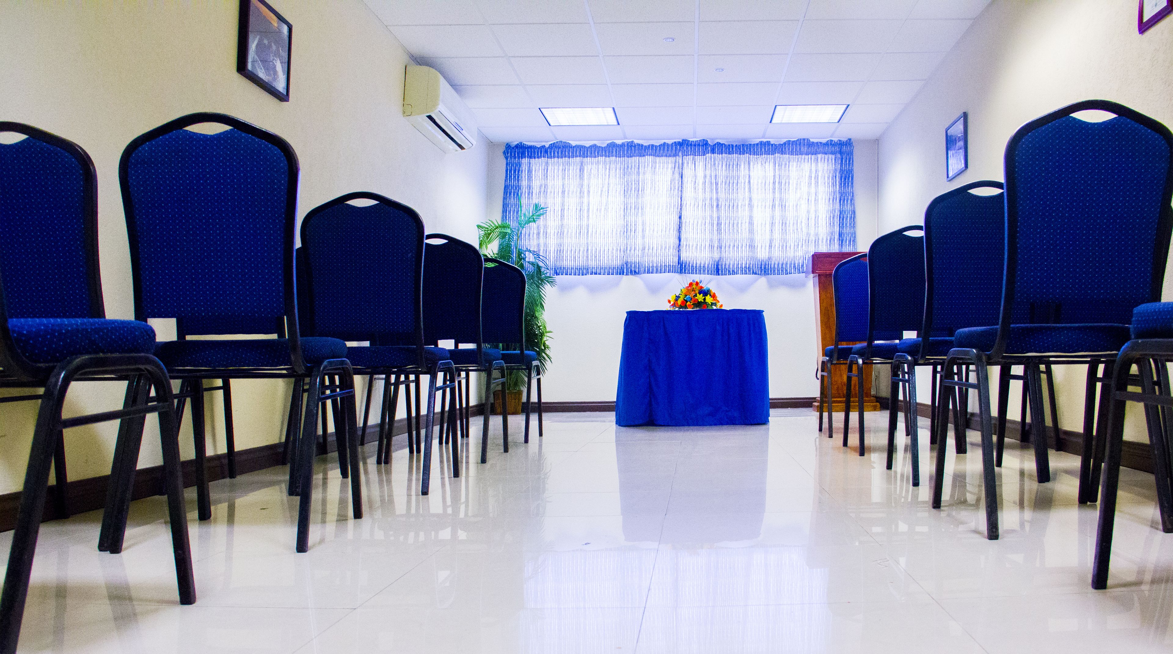 A conference room with rows of blue chairs, a podium, and a table with a blue tablecloth.