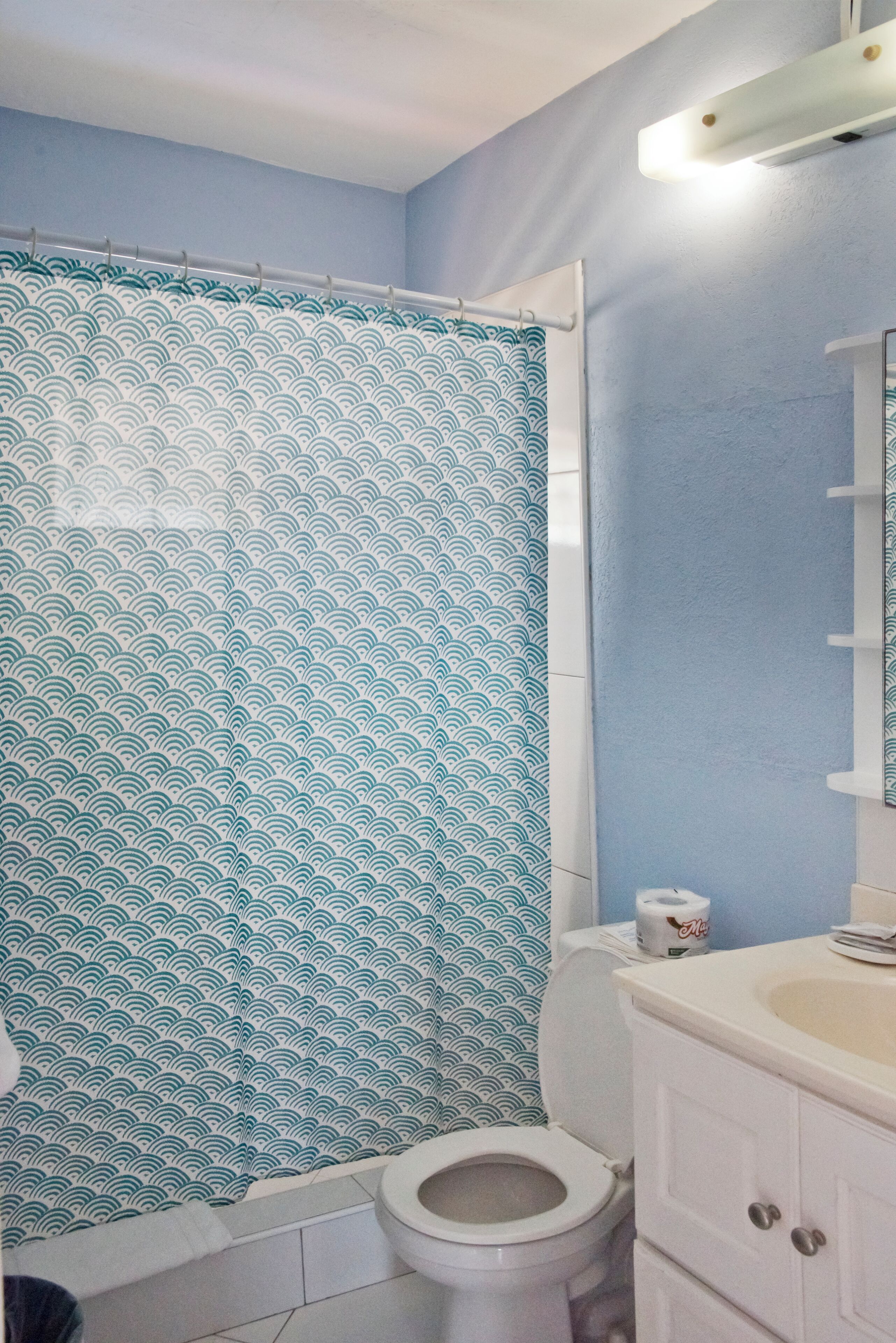 Een badkamer met douchegordijn met een golfpatroon, toilet en wastafel met spiegel erboven.