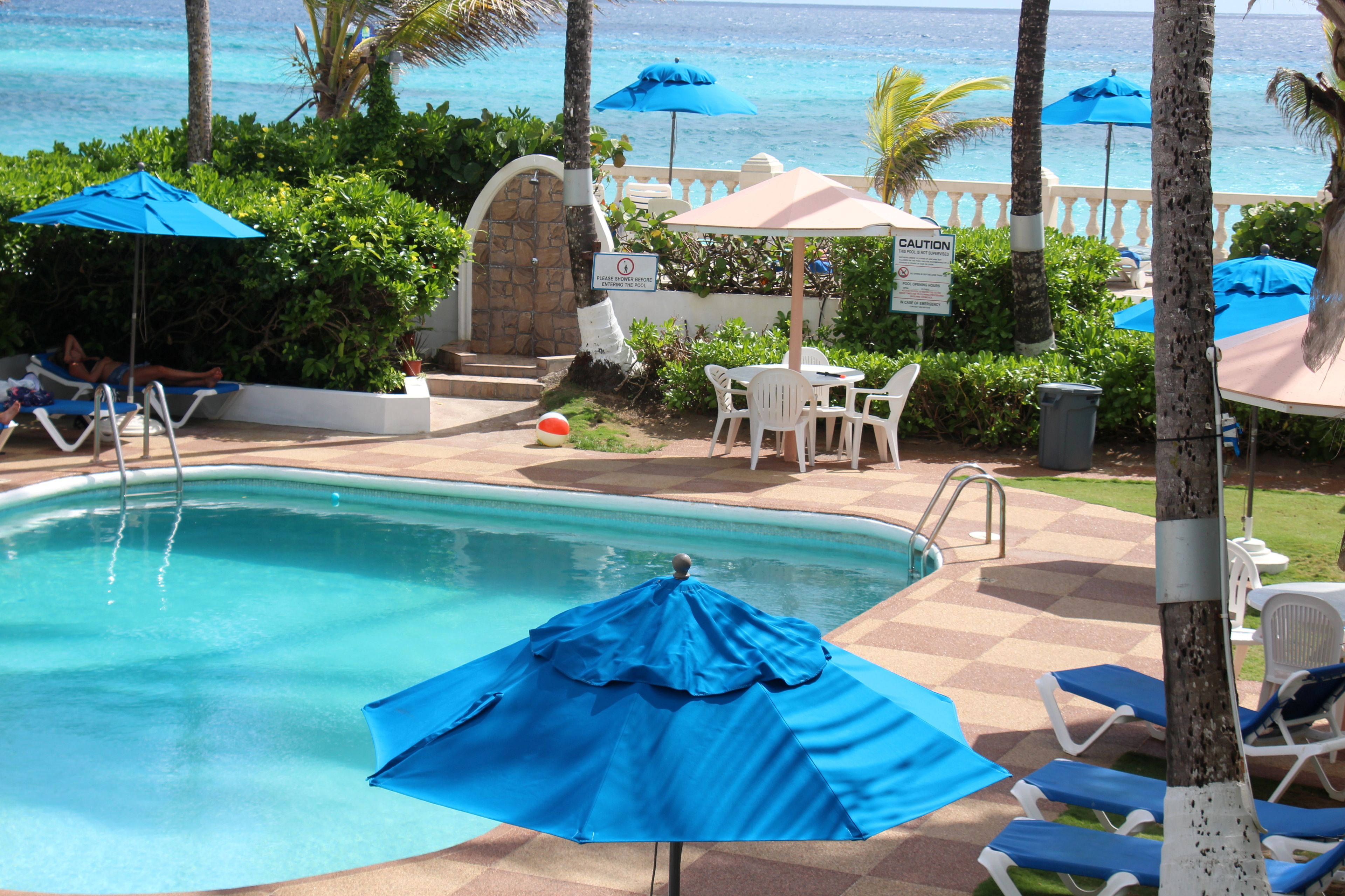 A pool area with blue umbrellas, lounge chairs, and a sign with caution tape.