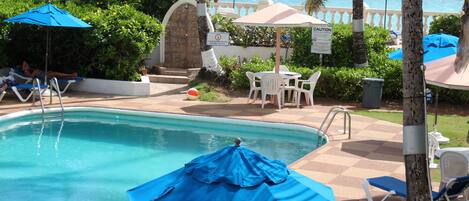 A pool area with blue umbrellas, lounge chairs, and a sign with caution tape.