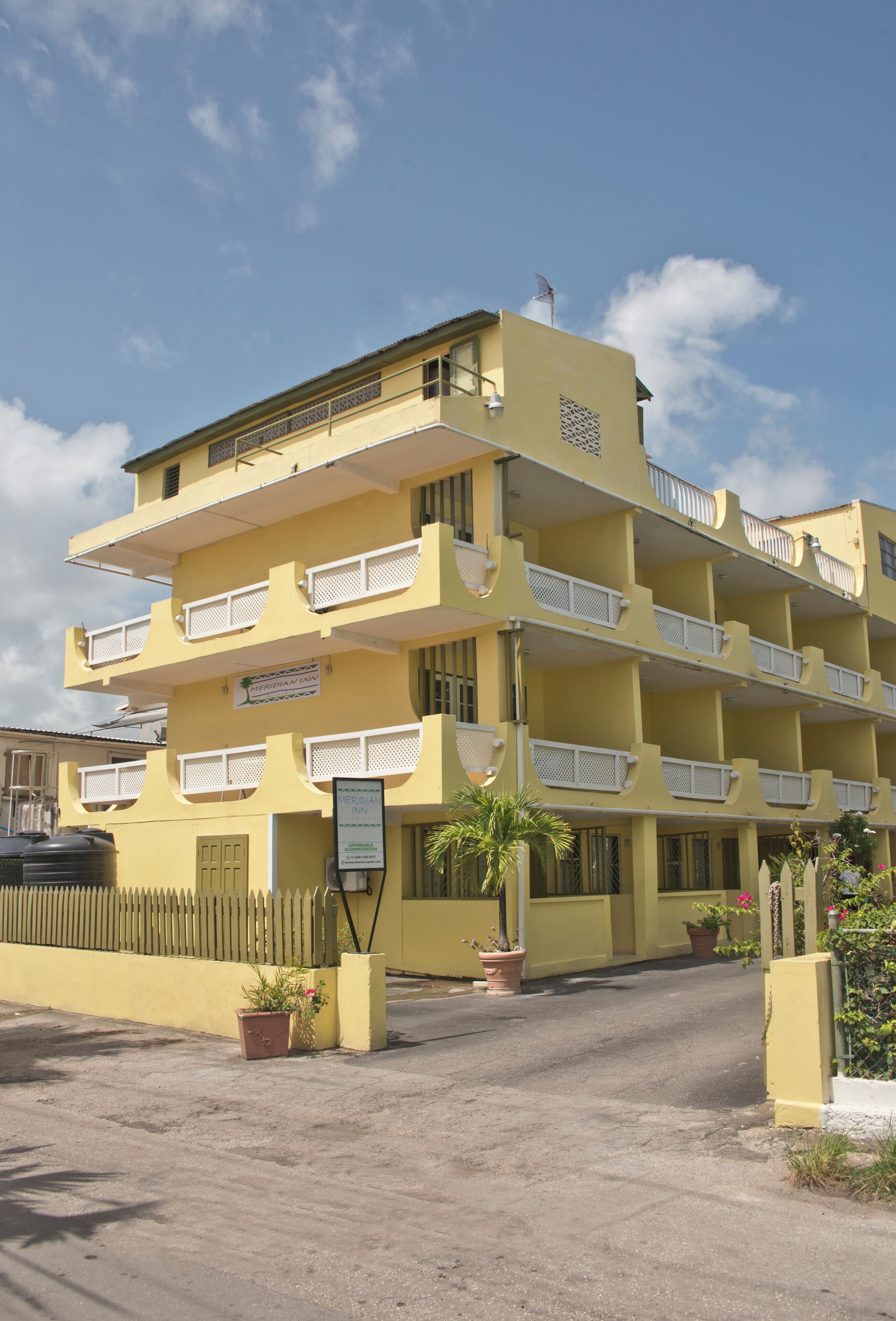 A multi-story yellow building with balconies, a signboard, and potted plants.