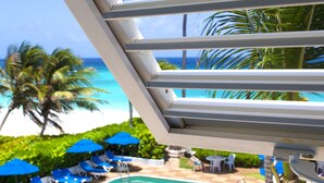 A pool area with blue umbrellas and lounge chairs, a clear view of the ocean, and palm trees. - Dover Beach Hotel (St. Lawrence Gap)
