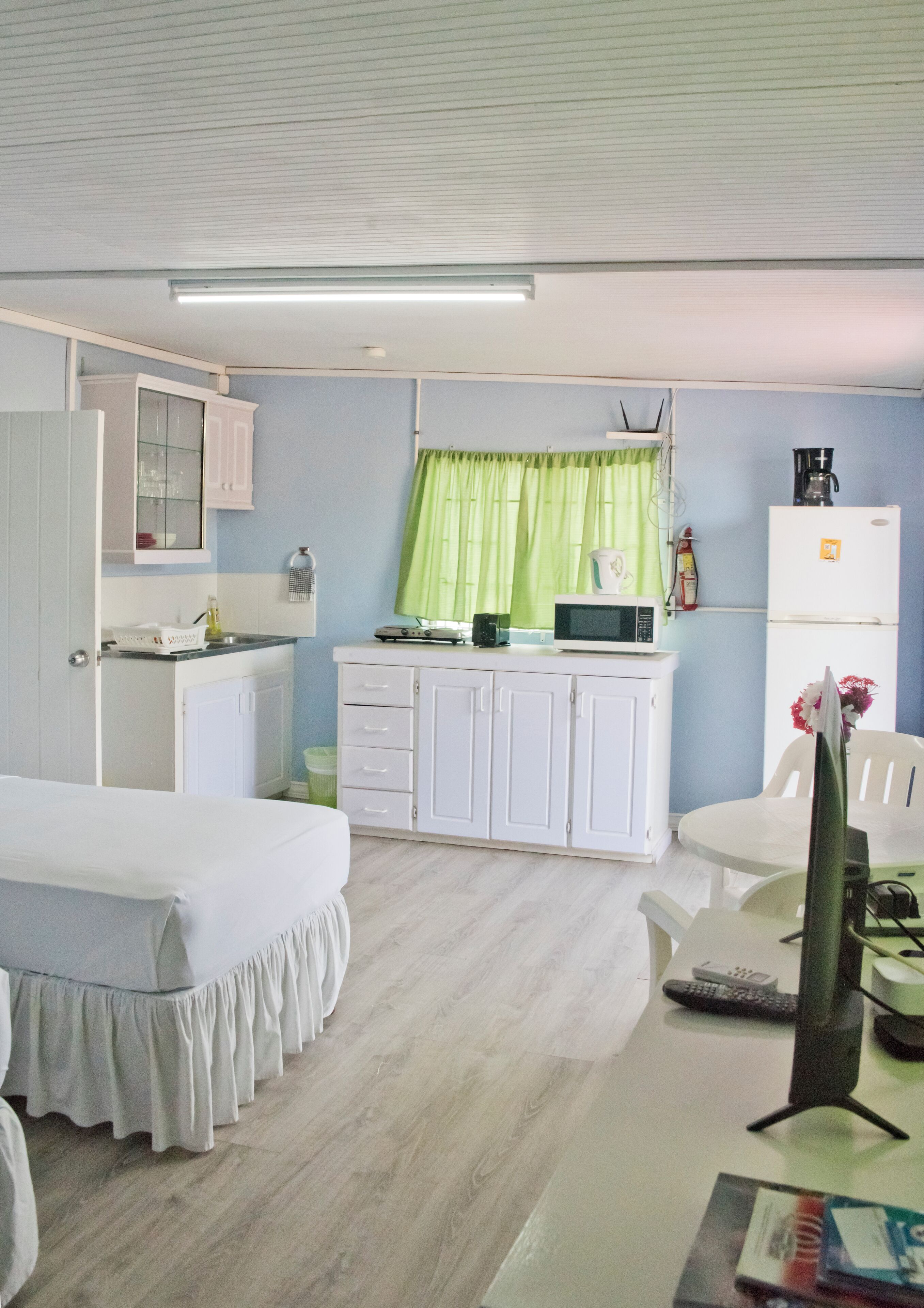 A compact room with a bed, a small kitchenette, a dining area, and a window with green curtains.