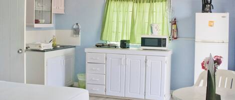A compact room with a bed, a small kitchenette, a dining area, and a window with green curtains.
