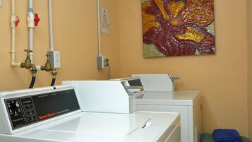 A laundry room with a front-loading washer and dryer, a wall-mounted faucet, and a colorful abstract painting.