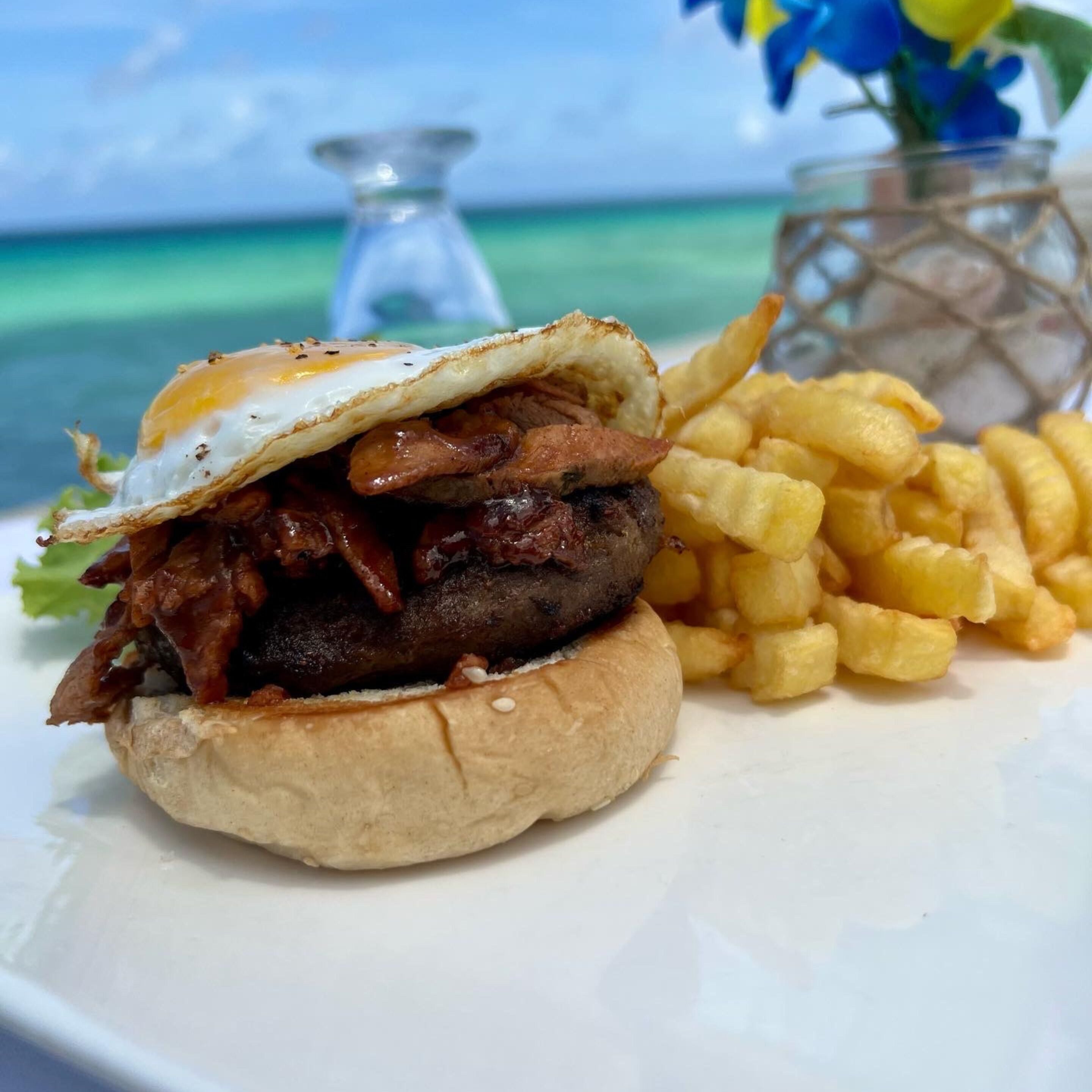 A sandwich with a fried egg on top, accompanied by a side of fries, on a white plate.