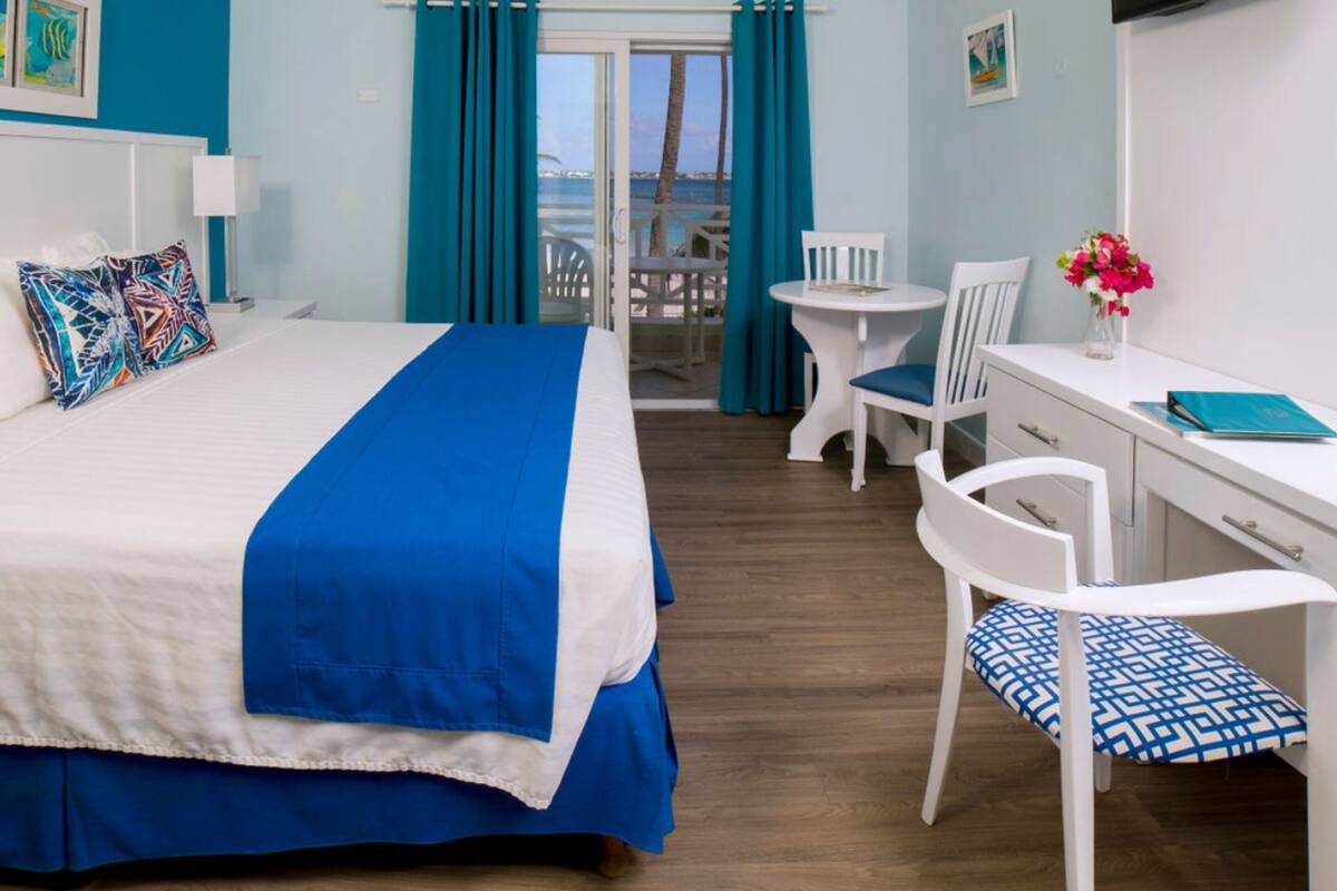Habitación de hotel con cama, escritorio, silla, televisor y vista al mar.