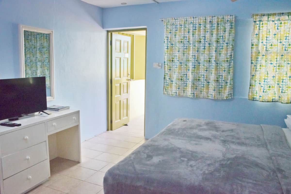 Un dormitorio con cama, escritorio con televisor y puerta que da a otra habitación.